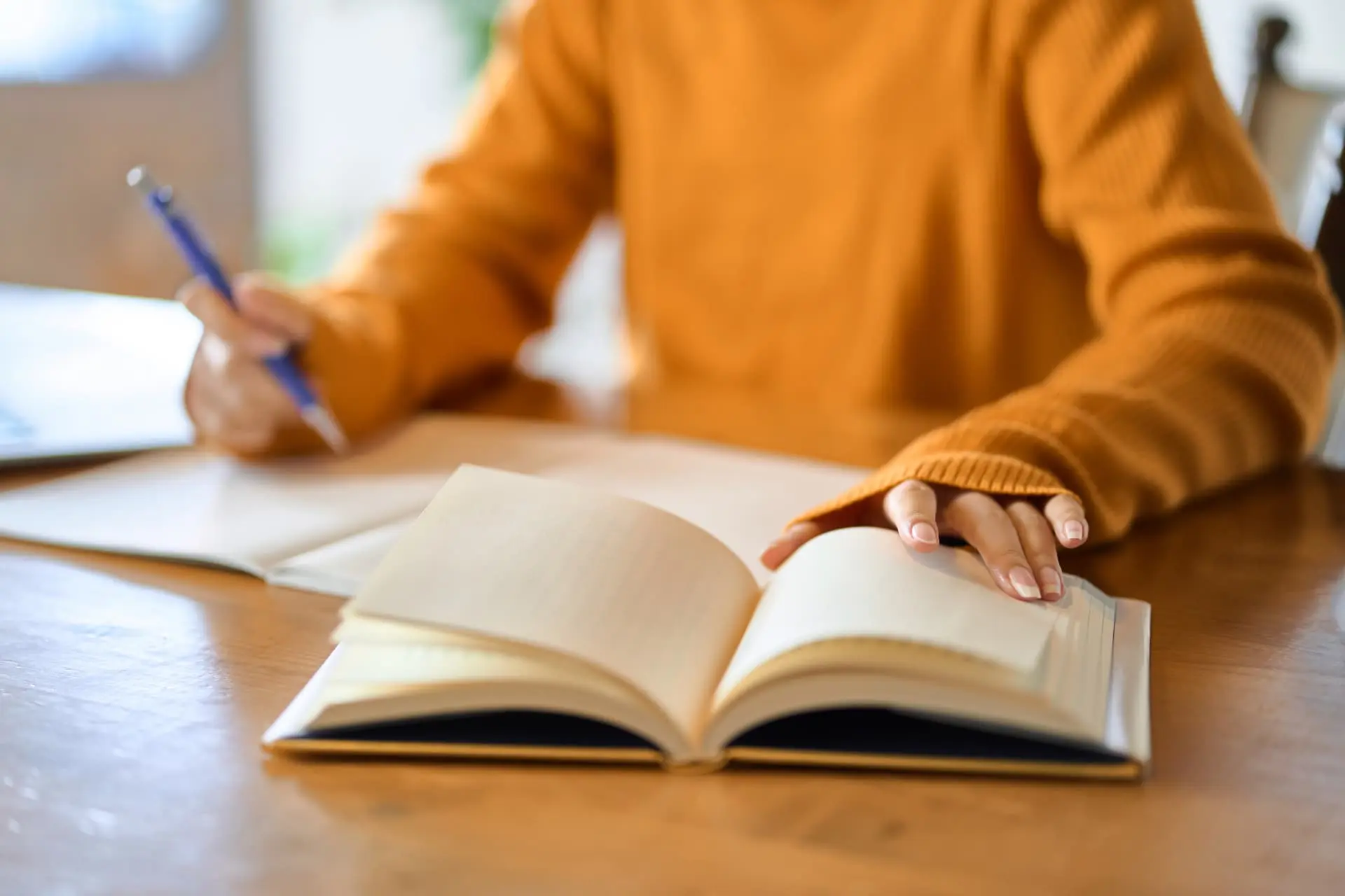 A student taking notes from an open textbook at a desk
